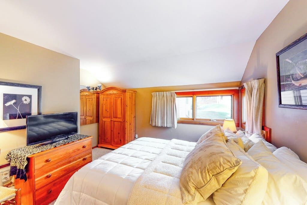 Une chambre à coucher avec un lit, un téléviseur posé sur une commode, une armoire et une fenêtre avec des rideaux.