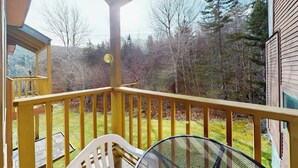 Une terrasse en bois avec une rambarde, une chaise blanche et une table.
