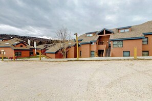 A building with multiple floors, a gravel parking area, and a staircase leading to the entrance. - Trail Creek second-floor condo with open views and game room access (Killington)