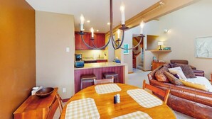 Un coin repas avec une table et des chaises en bois, une cuisine à l’arrière-plan et un salon avec un canapé.