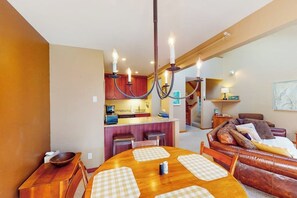Ein Essbereich mit Holztisch und Stühlen, im Hintergrund eine Küche und ein Wohnbereich mit einer Couch.
