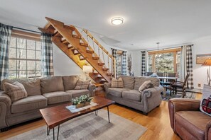 Ein Wohnzimmer mit zwei Sofas, einem Couchtisch, einer Holztreppe und einem Essbereich mit Tisch und Stühlen.