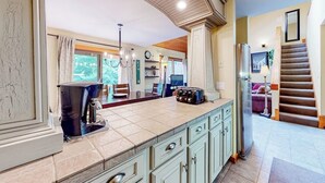 A spacious kitchen with a large island, a dining area with chairs, a staircase, and a living room with a sofa. - Trail Creek 33 | Condo in Killington (Killington)