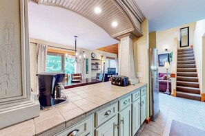 A spacious kitchen with a large island, a dining area with chairs, a staircase, and a living room with a sofa. - Trail Creek 33 | Condo in Killington (Killington)