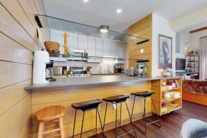 A modern kitchen with a glass partition, wooden bar stools, and a coffee machine. - Two-story condo with private sauna, pool, hot tubs & gym - walk to lifts (Killington)