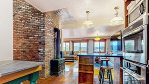 A kitchen with a brick wall, a wooden table, stools, and modern appliances. - Tranquil retreat with generous deck, fitness area, & amazing views (Pittsfield)