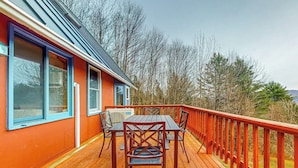 A wooden deck with a table and chairs, a red railing, and a building with blue-framed windows. - Tranquil retreat with generous deck, fitness area, & amazing views (Pittsfield)