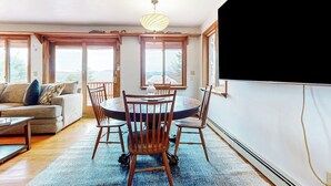 A dining area with a round table and chairs, a sofa, and large windows with a view. - Tranquil retreat with generous deck, fitness area, & amazing views (Pittsfield)