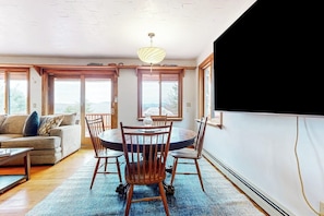 A dining area with a round table and chairs, a sofa, and large windows with a view.