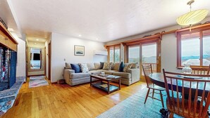 A spacious living room with a sofa, coffee table, and dining table. - Tranquil retreat with generous deck, fitness area, & amazing views (Pittsfield)