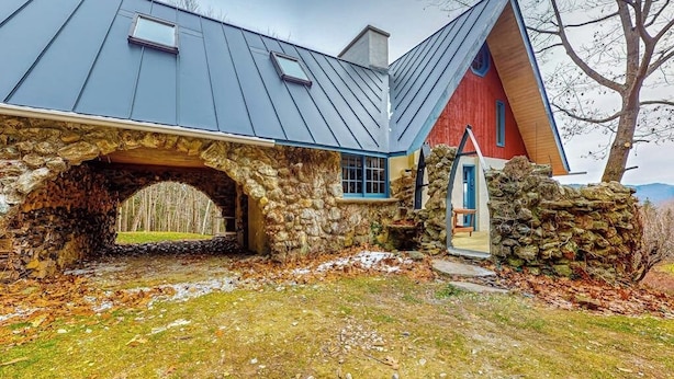 A stone archway leading to a house with a blue roof and a red door. - Tranquil retreat with generous deck, fitness area, & amazing views (Pittsfield)