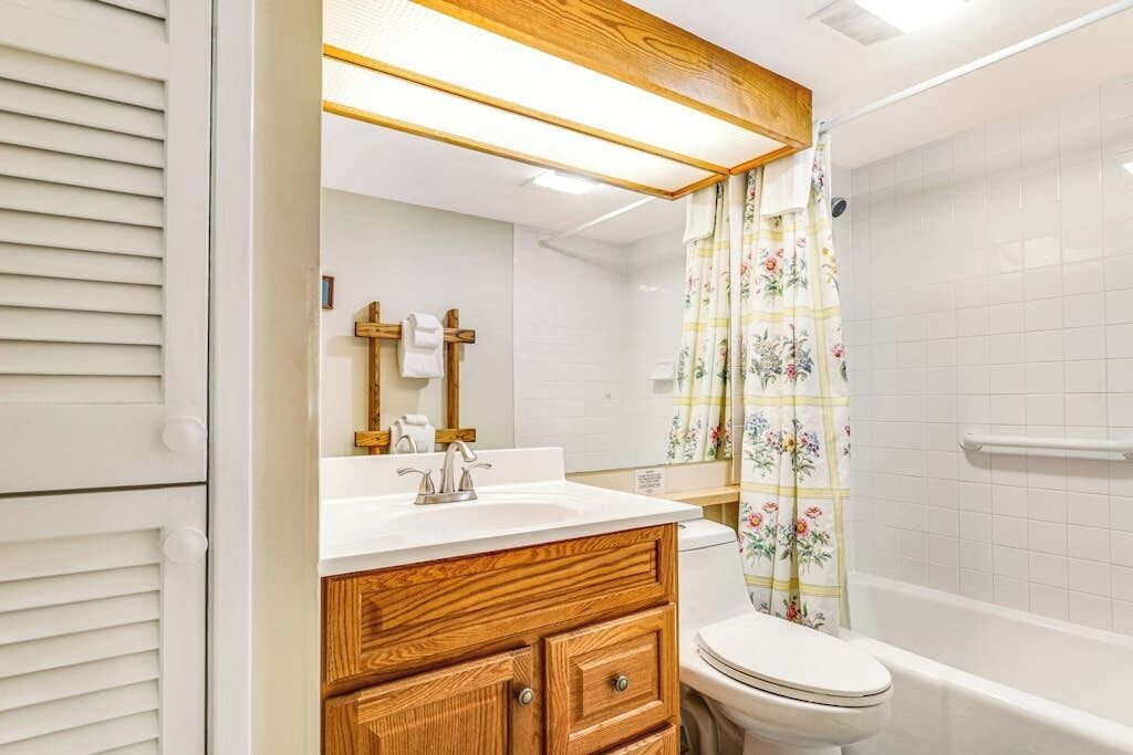 Un baño con tocador de madera, inodoro y ducha con cortina estampada.