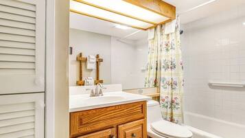 Un baño con tocador de madera, inodoro y ducha con cortina estampada.
