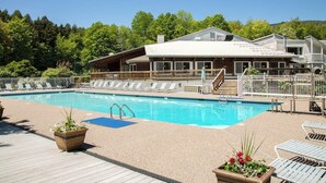 A swimming pool with lounge chairs, a wooden deck, and a building with large windows in the background. - Welcoming Condo with Shared Pools, Easy Access to Golf & Slopes (Warren)