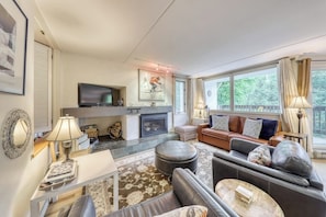 Ein Wohnzimmer mit Kamin, Sofa, Hocker und Fernseher.