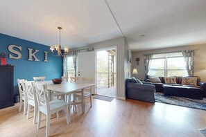 Ein modernes Wohnzimmer mit Essbereich, einer Kristallleuchtre und einem großen Fenster mit Vorhängen.