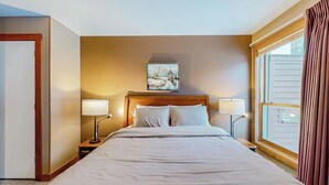 Hotellihuone, jossa on suuri sänky, kaksi yöpöytää valaisimineen, taulu seinällä ja ikkuna, jossa on verhot.