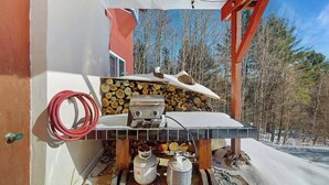 En utomhusgrill med en eldstad, propantankar och en röd slang.
