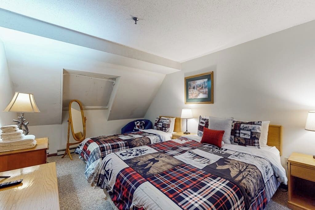 A bedroom with two beds, a mirror, a desk, and a framed picture on the wall.