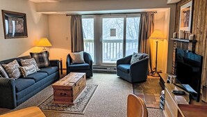 Un salon chaleureux avec un canapé, deux fauteuils, une table basse en bois, un téléviseur et une cheminée.