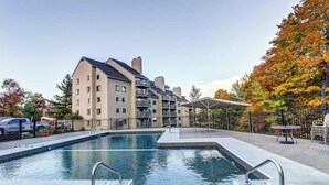 Une piscine avec un jacuzzi, entourée d’un bâtiment doté de balcons et d’un espace clos aménagé avec des chaises.