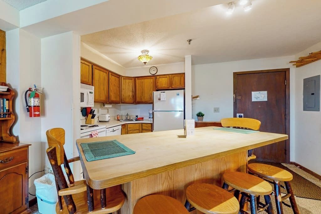 Une cuisine avec des meubles en bois, un îlot central doté de tabourets, un four à micro-ondes et un réfrigérateur.