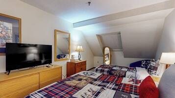 A bedroom with a television, dresser, bed with a plaid bedspread, and a mirror.
