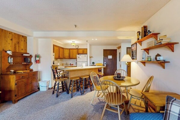 A compact kitchen with wooden cabinets, a central island with stools, and a dining table with chairs.