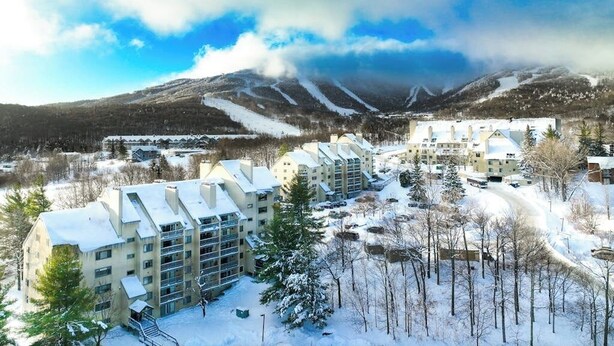 Un quartier résidentiel enneigé, avec des immeubles à plusieurs étages, une piste de ski en arrière-plan et un ciel dégagé.