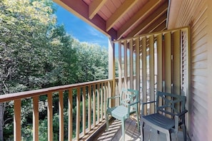 A balcony with wooden railings, two chairs, and a view of dense trees. - Top-Floor Condo, ski-home trail, w/ fireplace, balcony, w/d, hot tub, pool, wifi (Killington)