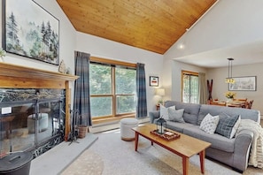 A living room with a fireplace, a sofa, a coffee table, and a large window. - Top-Floor Condo, ski-home trail, w/ fireplace, balcony, w/d, hot tub, pool, wifi (Killington)