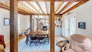 A dining area with wooden beams, a chandelier, and a view into the kitchen. - Charming dog-friendly home with private deck, firepit, washer/dryer, & cable (Wallingford)