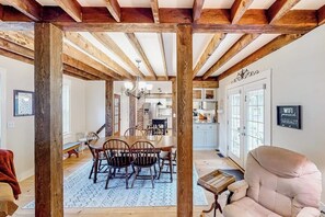 A dining area with wooden beams, a chandelier, and a view into the kitchen.
