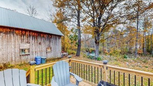 A wooden deck with Adirondack chairs, a metal railing, and a rustic barn in the background. - Charming dog-friendly home with private deck, firepit, washer/dryer, & cable (Wallingford)