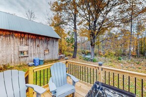 A wooden deck with Adirondack chairs, a metal railing, and a rustic barn in the background.