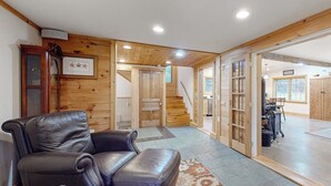 A room with a leather sofa, wooden walls, a staircase, and a view into another room. - Cozy house in the woods, riverfront, trail,  fireplace, wifi, w/d, bbq, balcony (Moretown)