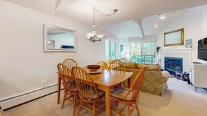 Ein Essbereich mit Holztisch und -stühlen, einer Chandelierleuchtre und einer Couch im Hintergrund.
