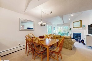 Ein Essbereich mit Holztisch und -stühlen, einer Chandelierleuchtre und einer Couch im Hintergrund.