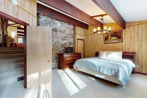 Ein Schlafzimmer mit Bett, Holzwänden, einer Steinwand, einer Chandelüster und einem Gemälde.