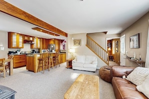 A spacious living area with a kitchen, a white sofa, a brown leather couch, and a wooden coffee table. - Cozy, updated riverfront home with gas stove & AC (Warren)