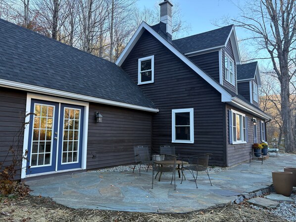A two-story house with a stone patio, a front door with glass panels, and a chimney.