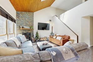 Una sala de estar moderna con una chimenea de piedra, un televisor montado en la pared y una escalera que sube a otro nivel.