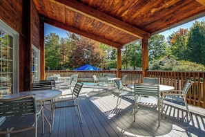 A covered outdoor deck with wooden beams, metal chairs, and tables, overlooking a pool and trees. - Relaxing Ski Condo with Pools and Entertainment - Near Ski Access (Warren)