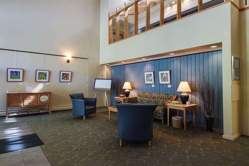 Eine Lobby mit hoher Decke, einer blauen Wand mit gerahmten Bildern, einem Sofa, zwei Lampen, einem Holzschrank und einem kleinen Tisch.