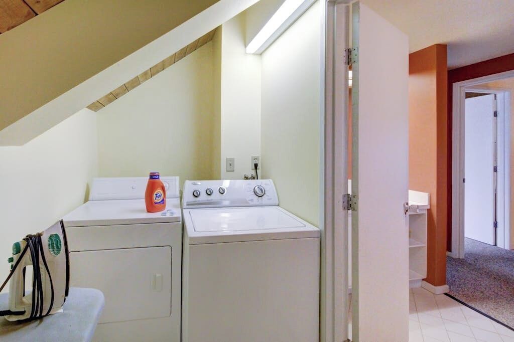 A laundry room with two washing machines, a dryer, and a bottle of detergent.