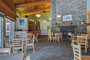 A cozy dining area with wooden tables and chairs, a stone fireplace, and a ceiling fan. - Relaxing Ski Condo with Pools and Entertainment - Near Ski Access (Warren)