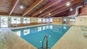 An indoor swimming pool with wooden beams, clear windows, and a tiled floor. - Lovely condo near skiing with 3 pools, sauna, fitness room & balcony (Warren)