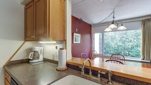 A kitchen with wooden cabinets, a coffee maker, a sink, and a window with a view of trees. - Lovely condo near skiing with 3 pools, sauna, fitness room & balcony (Warren)