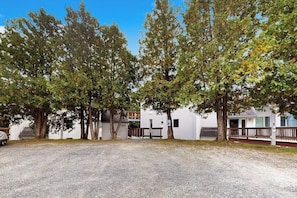 A gravel parking area with trees and a white building with a porch.