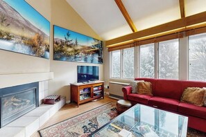 Ein Wohnzimmer mit Kamin, rotem Sofa, großen Fenstern und Kunstwerken an den Wänden.